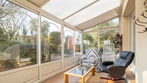 A conservatory with a glass ceiling, a wooden coffee table, a patterned armchair, and a black leather chair. - Holiday Home 'Grande Maison À 5min Des Plages' with Shared Pool, Terrace and Private Garden (Pouldreuzic)