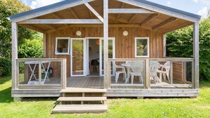 Eine Holzhütte mit überdachter Veranda, zwei Fenstern und einem umzäunten Deckbereich.