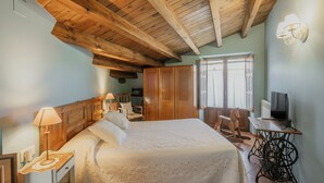 Un dormitorio con techo de madera, una cama con colcha, una mesita de noche, una silla, un armario y una máquina de coser.