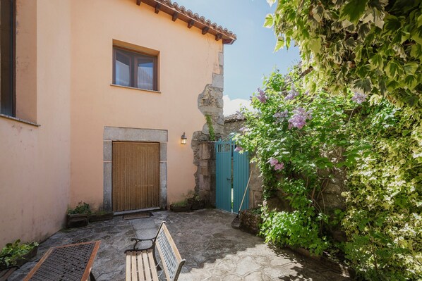 A stone-paved courtyard with a bench, a wooden door, and a blue gate.