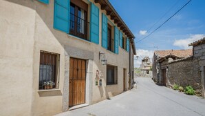 Una calle estrecha con un edificio que presenta una puerta de madera, una ventana con una cesta de flores y una pared de piedra.