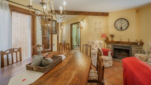 Comedor con mesa de madera, sillas, candelabro, chimenea y un reloj en la pared.