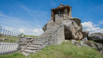 Une structure en pierre avec un escalier menant à un petit bâtiment situé en haut, entourée de gros rochers et d’une clôture métallique.