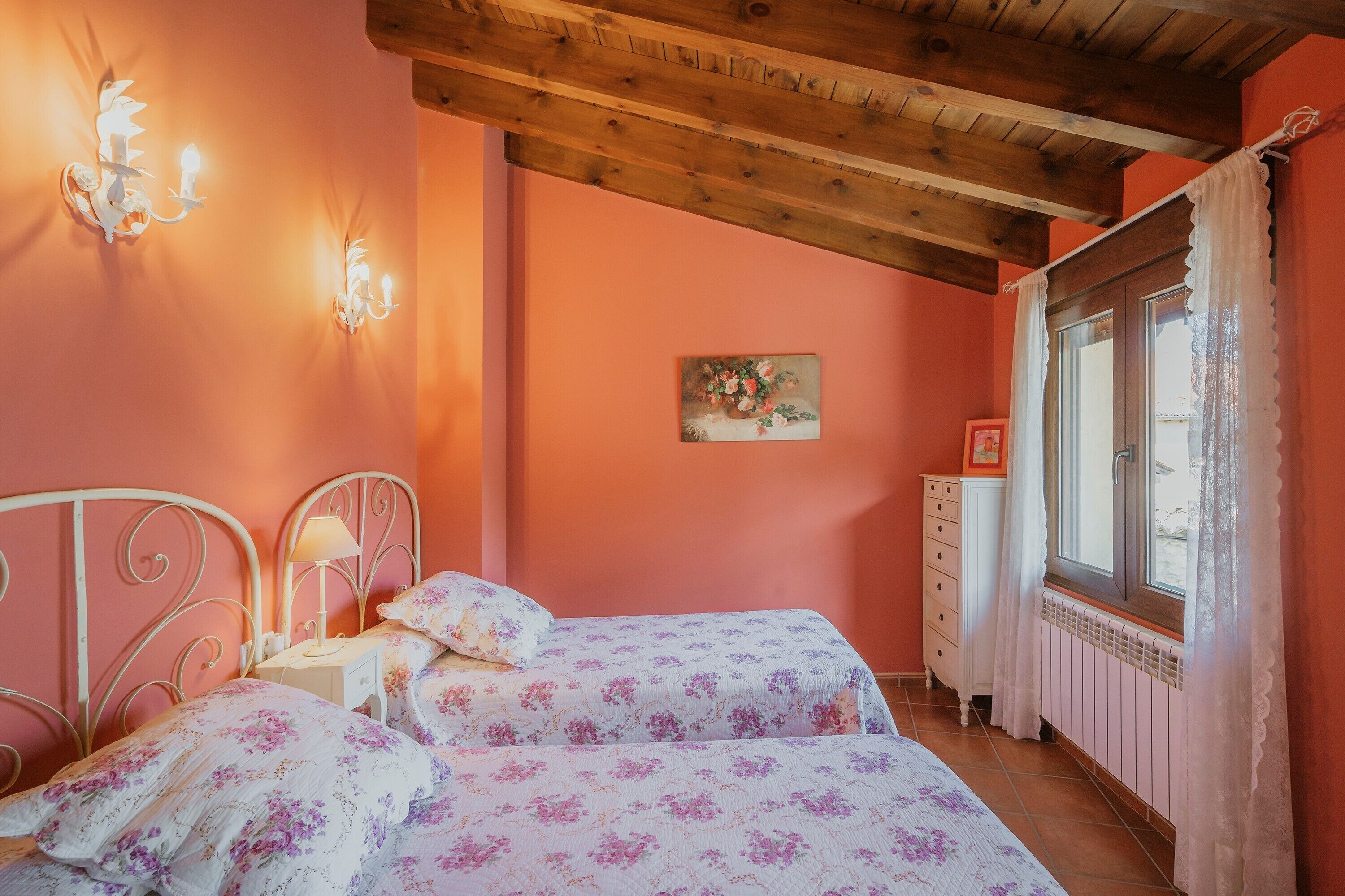 Une chambre avec deux lits, une table de chevet, une commode, une fenêtre avec des rideaux et un plafond en bois.