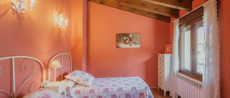Une chambre avec deux lits, une table de chevet, une commode, une fenêtre avec des rideaux et un plafond en bois.