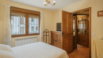 A bedroom with a bed, a wooden dresser, a radiator, a television, and a chandelier.