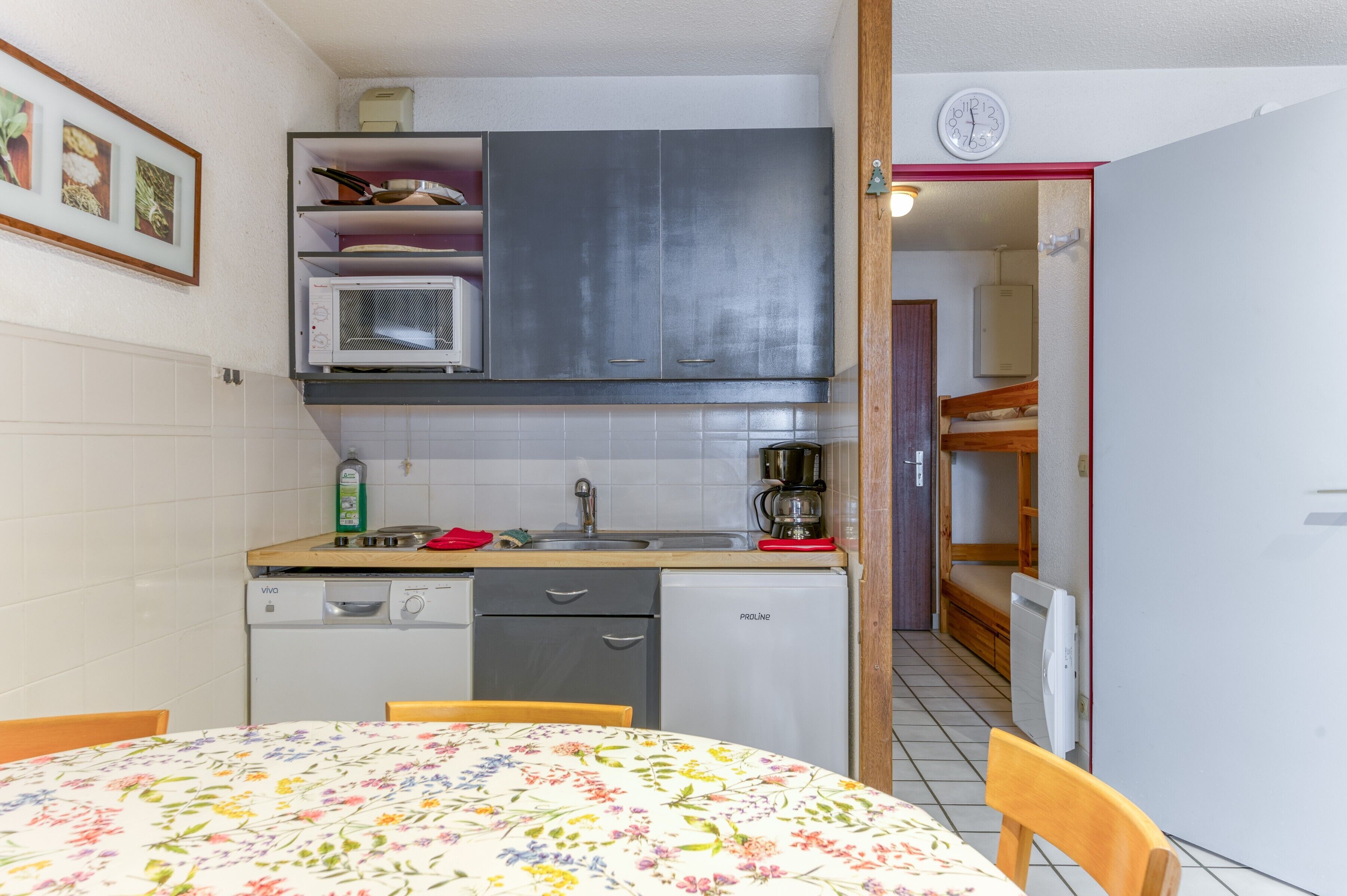 A compact kitchen with a microwave, sink, and a dining area with a floral tablecloth.