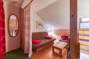 Una habitación acogedora con suelo de madera, un sofá marrón con cojines rojos, una mesita y un espejo en la pared.