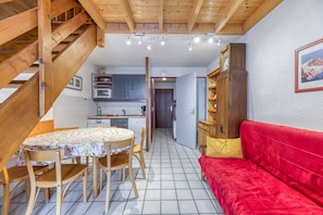 A kitchen with a microwave, a wooden staircase, a dining table with chairs, and a red sofa.