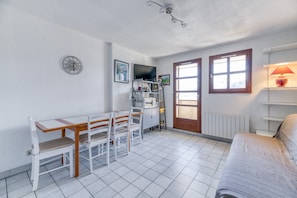 Een kamer met een eettafel, stoelen, een televisie, een radiator en een bank.