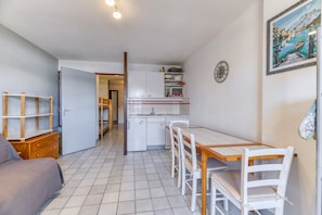 Et lille køkken med hvide skabe, et spisebord med stole og en trækommode.