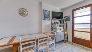 A room with a wooden table and chairs, a clock, a television, and a window with a mountain view. - Apartment 'Granges 9 - Vue' with Mountain View and Balcony (Villard-Reculas)