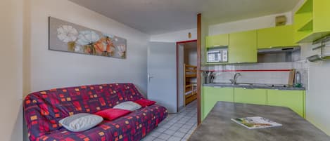 Um espaço de estar compacto com sofá, mesa, cozinha e porta que dá para outro quarto.