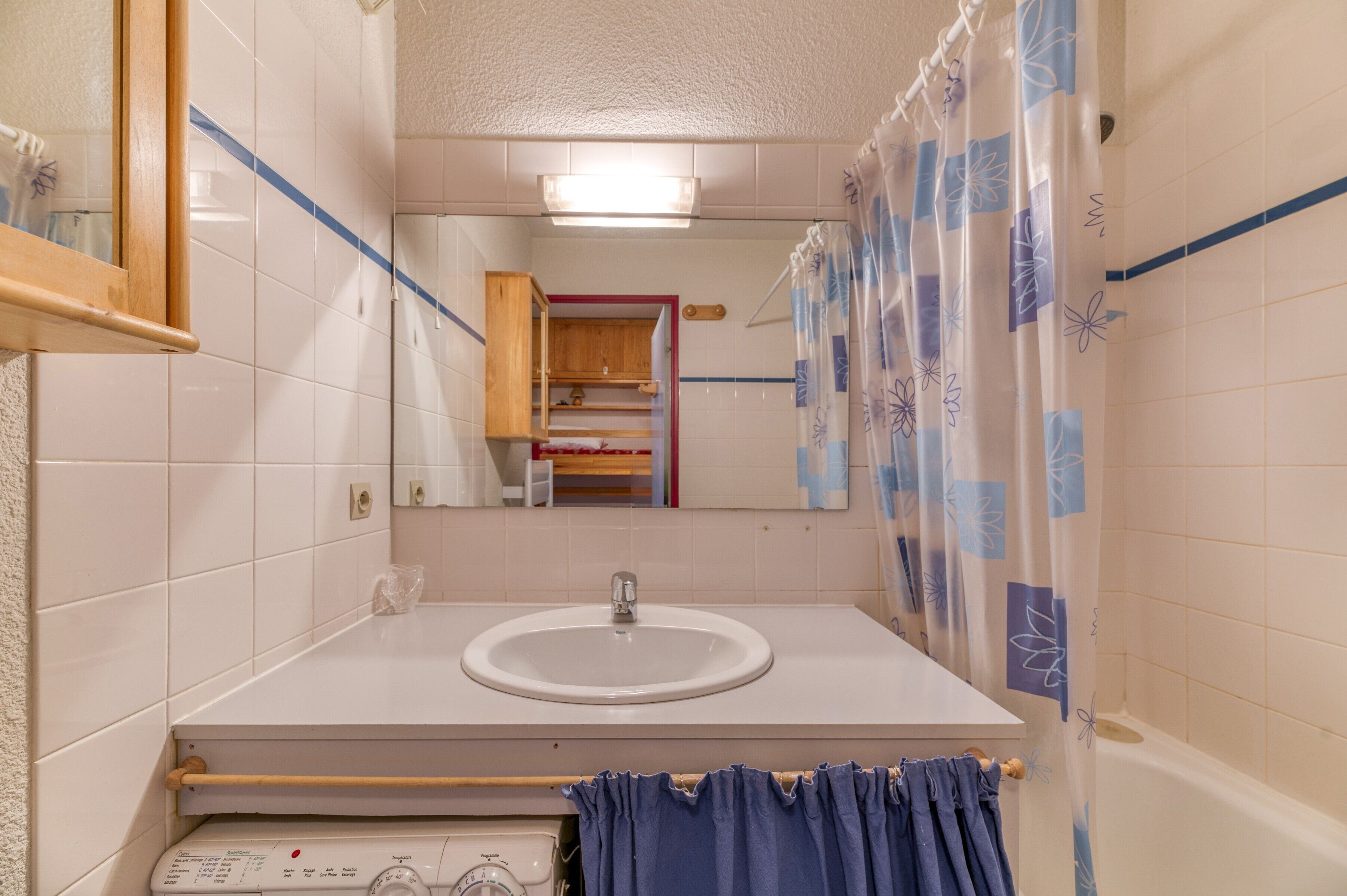 Ein Badezimmer mit weißem Waschbecken, einem Spiegel, einem Holzkabinet und einer Duschvorhang.
