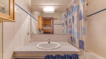 Ein Badezimmer mit weißem Waschbecken, einem Spiegel, einem Holzkabinet und einer Duschvorhang.