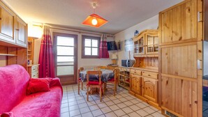 Una cocina compacta con armarios de madera, una mesa de comedor con sillas, un sofá rojo y un televisor.