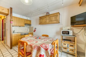 Una cocina compacta con armarios de madera, microondas y una mesa con mantel a cuadros.