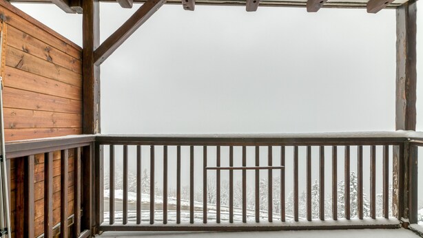 Ein hölzerner Balkon mit Metallgeländer, mit Blick auf eine verschneite Landschaft.