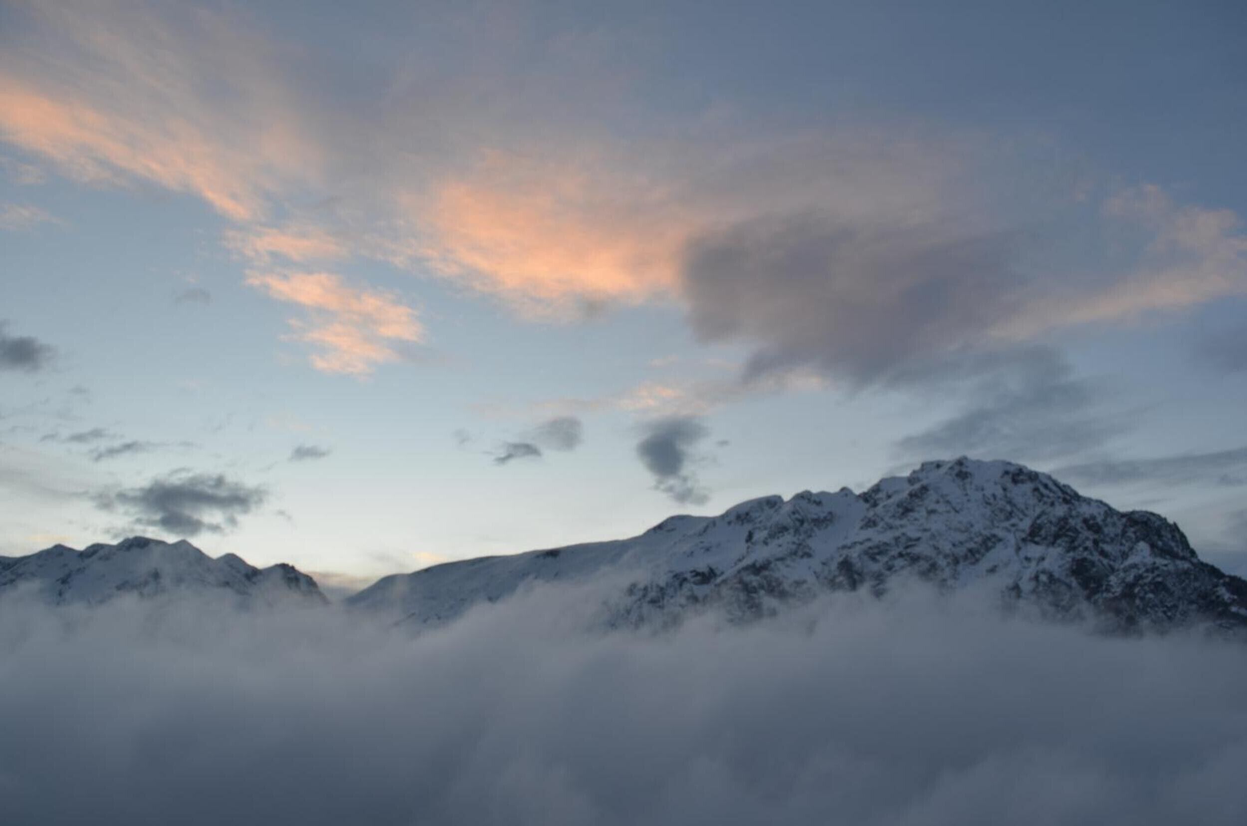 A mountain range with snow-covered peaks and clouds at the base.
