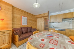 Acogedora habitación de estilo cabaña con interiores de madera, una mesa de comedor con mantel estampado, un sofá y una zona de cocina con armarios de madera y una estufa.