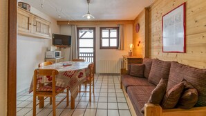 Ein gemütliches Zimmer mit Holzboden, einem Esstisch mit Stühlen, einer Couch, einem Fernseher und einem gerahmten Bild an der Wand.