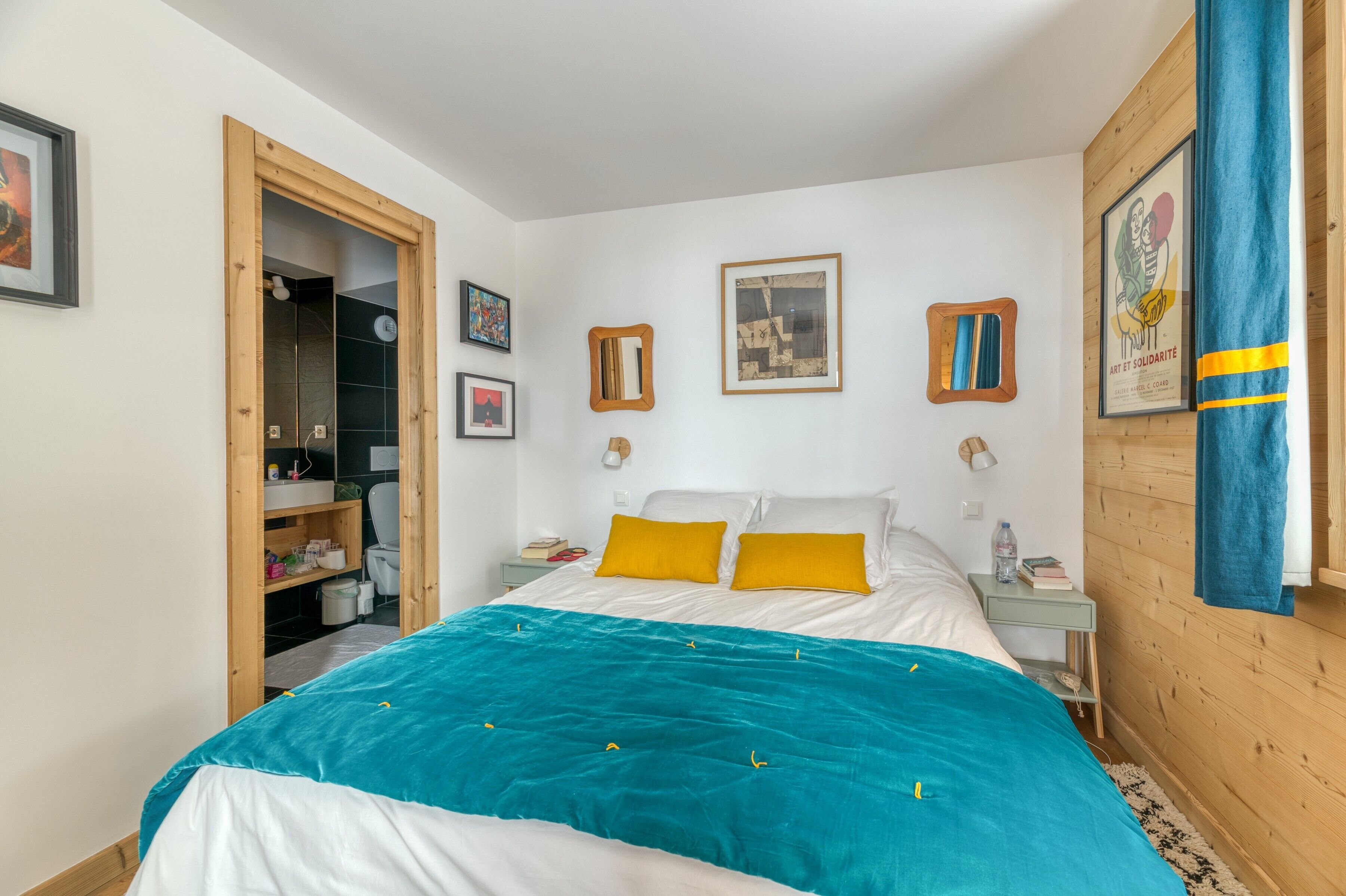 Un dormitorio con cama, mesitas de noche, un armario y una puerta que da a un baño.