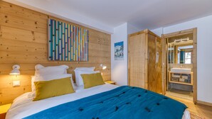 Un dormitorio con cabecera de madera, cama con cubrecama azul, dos lámparas de noche, un cuadro abstracto de colores y un armario de madera.