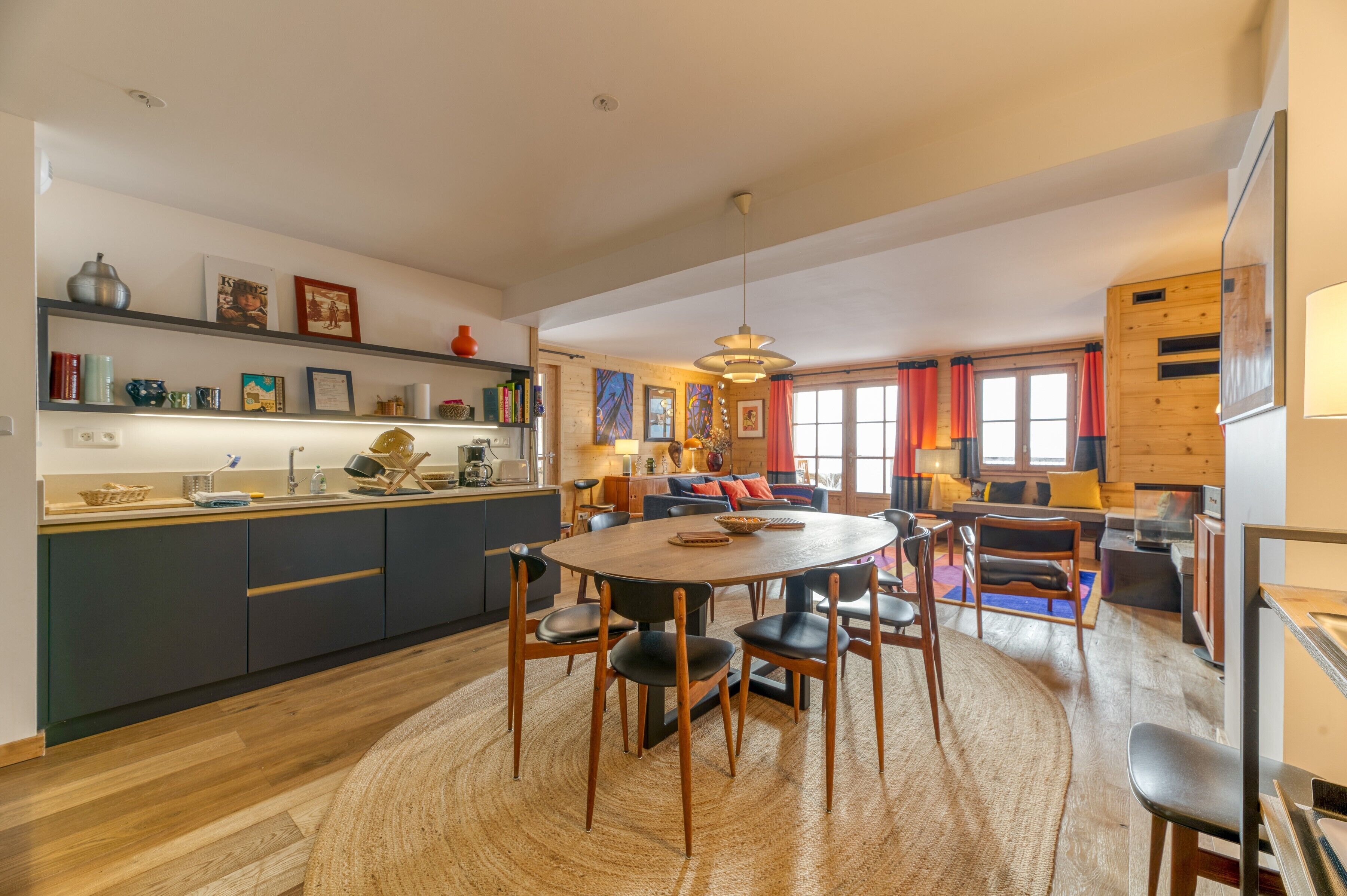 Une cuisine moderne avec un coin repas, un plancher en bois et une grande fenêtre agrémentée de rideaux.