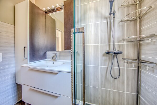 A modern bathroom with a glass-enclosed shower, a white sink, and a large mirror.