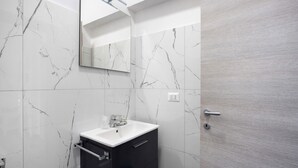 A bathroom with a marble wall, a sink, a mirror, and a door. - Room 'Al Corso Suite' with Balcony, Wi-Fi and Air Conditioning (Salerno)