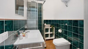 Une salle de bain avec une douche à parois de verre, un lavabo blanc, des toilettes et une étagère contenant des articles de toilette.