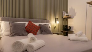 Une chambre d’hôtel comprenant un lit, des oreillers, des serviettes, une table de chevet, une lampe et une étagère avec divers objets.