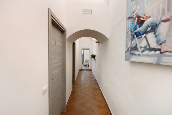 A hallway with a tiled floor, a white door, a white wall, and a painting.