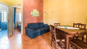 A dining area with a wooden table and chairs, a blue sofa, and a wall with a mural of birds.