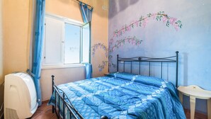 A bedroom with a bed, a radiator, a window with curtains, and a wall with a floral mural.