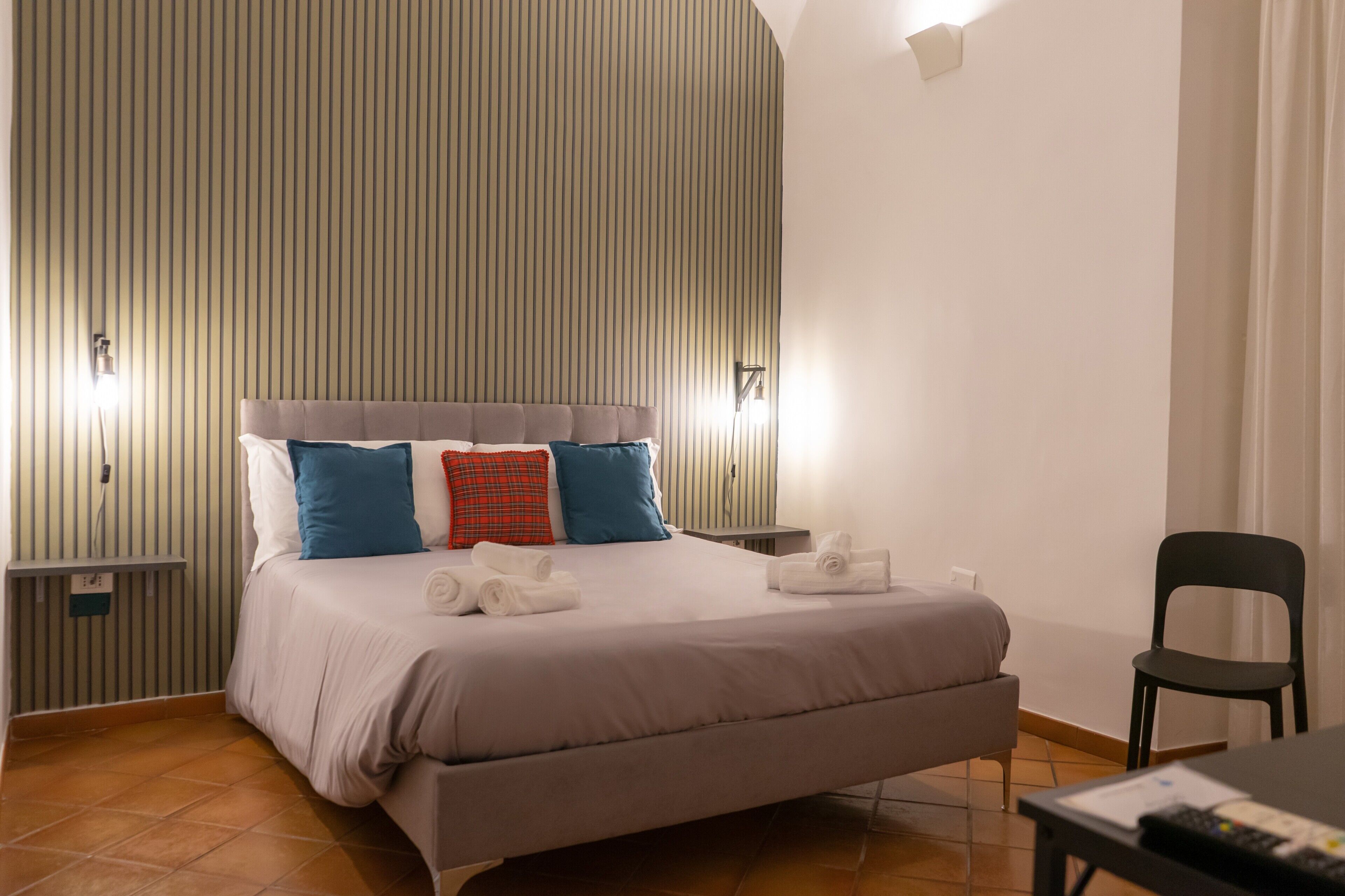 Une chambre d’hôtel avec un grand lit, une chaise, une table et un luminaire fixé au mur.