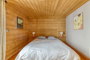 A wooden-paneled room with a bed, two bedside lamps, a poster on the wall, and a framed artwork. - Chalet 'Le Flocon Grand  4 Étoiles' with Mountain View, Private Terrace and Wi-Fi (Villard-Reculas)