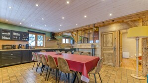 Een keuken met een eettafel, stoelen, kastjes en een houten plafond.
