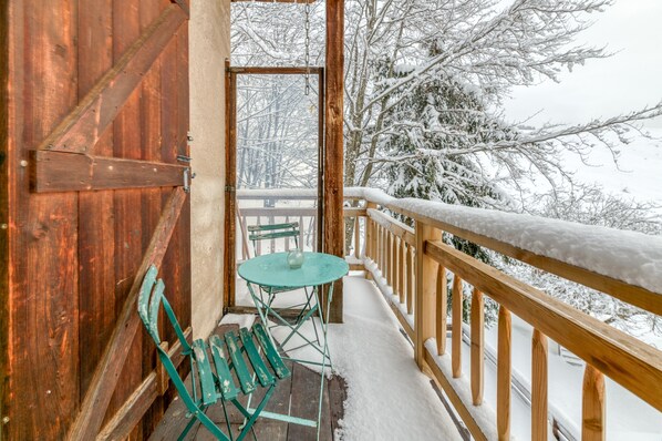 Varanda de madeira com mesa e cadeiras, árvores cobertas de neve e guarda-corpo de madeira.