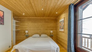Een kamer met houten lambrisering, een bed, twee nachtkastjes en een raam met gordijnen.