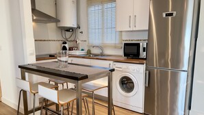 Ett modernt kök med ett kylskåp i rostfritt stål, en inbyggd tvättmaskin, en mikrovågsugn och en varmvattenberedare.