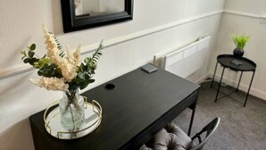 Une pièce comprenant une console noire, un vase avec des fleurs blanches, un miroir au mur, un radiateur et une petite table ronde sur laquelle est posée une plante.