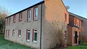 Un bâtiment à deux étages, doté d’un toit en pente, de nombreuses fenêtres à cadre rouge et d’une antenne parabolique sur le toit.