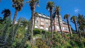 A large building with multiple floors, surrounded by lush greenery and palm trees. - "Ti Roz" 3-star Apartment with Sea View, Direct Beach Access and GR34 (Perros-Guirec)