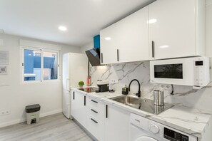 A modern kitchen with white cabinets, a built-in microwave, a stainless steel sink, and a dish drying rack.