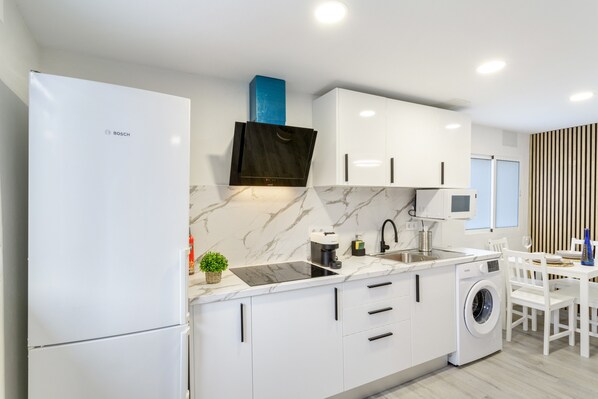 A modern kitchen with white cabinets, a Bosch refrigerator, a built-in washing machine, and a dining area with a white table and chairs.