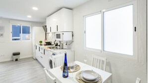 A modern kitchen with white cabinets, a microwave, and a dining area with a table set for two. - Vacation Home 'Magma' with Private Terrace, Private Garden and Wi-Fi (Santa Brígida)
