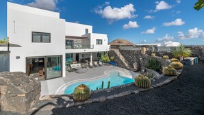 Un edificio moderno blanco con piscina, mobiliario exterior y cactus.