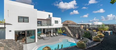 A modern white building with a swimming pool, outdoor seating, and cacti.