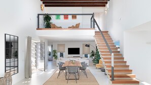 Un salón amplio con una mesa de comedor, sillas, un sofá, una escalera y un televisor grande.